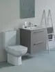 Weißes WC mit platzsparendem Design und grauer Waschbeckenkombination. Ideal Standard Armatur auf der Ablage. Helle Wand und Leiter im Hintergrund.